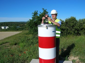 Measurements for ITER's primary survey network have an accuracy of 1 mm. David Wilson adjusts equipment on one of the eleven survey monuments positioned around the ITER platform. (Click to view larger version...)